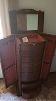 Jewelry armoire open with side cabinet doors open showing multiple hooks on both doors for hanging necklaces or bracelets, the main body with pull-out drawers and a lock on the top drawer.