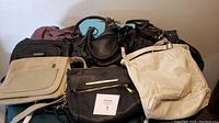 Photo showing 10 assorted purses of various colors including black, white, beige, brown, and turquoise, mostly handbags of different styles and sizes arranged on a cloth.