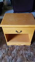 Front view of the wooden nightstand showing drawer with metal handle and open shelf below.