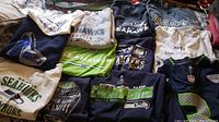 Wide view of 13 pieces of Seattle Seahawks shirts, sweatshirts, jersey, and one hat arranged together