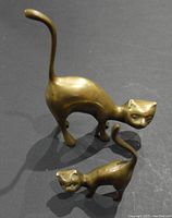 Two brass cat figurines together, showing height and shape difference.