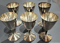 Front and angled view of 4 silverplate wine goblets grouped together, showing their shape and reflective surfaces with signs of wear.