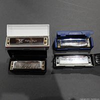 Four various harmonicas with cases placed on a flat surface, showing differences in design and condition.