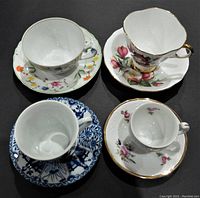 Top view of four tea cups with matching saucers showing various floral and patterned designs and gold accents