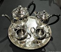 Full view of the silverplate tea service set on the round serving tray including teapot, coffee pot, creamer, and sugar bowl.