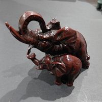 Two resin elephant figurines with detailed texture and dark brown finish, showing one larger and one smaller elephant with raised trunks