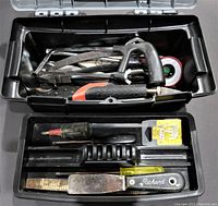 View of the open black toolbox showing assorted hand tools including a coping saw, crimping tool, putty knife, and small screwdriver.