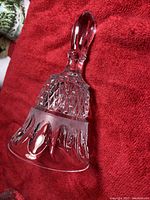 Clear crystal bell with diamond cut pattern and faceted handle lying on red fabric