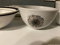 Close-up of the white porcelain soup bowl showing black floral dandelion-like pattern on one side.