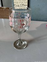 Clear wine glass with red 'Ho ho ho' text and white snowflake design on a table