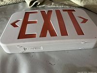 White exit sign with red 'EXIT' lettering and left and right arrows, viewed from an angle showing top and side with mounting bracket visible underneath.