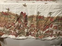 Close-up photo showing detailed fall-themed pattern featuring countryside houses with red roofs, pumpkins, and autumn leaves along border of tablecloth.