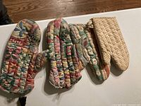 Quilted oven mitts seen from front on white table.