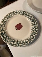 Photo of a vintage ceramic plate with textured green floral border and a red apple motif in the center.