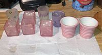 Nine assorted Yankee Candle candle holders including four pink square heart-pattern holders, three floral/butterfly glass holders, and two pink-striped ceramic teacup holders arranged on paper towels on a countertop.
