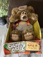 Front view of Rufus Jr. Country Bear teddy bear in original box, showing outfit and facial details