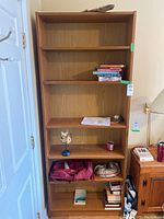 Full view of tall wood veneer book shelf with several items on shelves, showing the overall structure and condition.