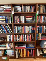 Front view of wood veneer Ikea bookshelf filled with many hardcover and paperback books. Bookshelves are filled with books arranged vertically and horizontally on five shelves.