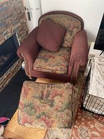 Overview of armchair with floral cushions and matching ottoman on floor, showing overall wear and fabric pattern.