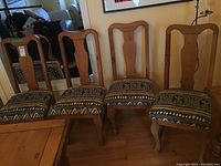 Four solid wood chairs with upholstered seats, patterned fabric cushions, and gently curved front legs, arranged in a row.