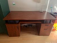 Front view of the wooden desk showing cabinet on left, drawers on right, and empty desktop surface with lamp.