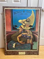 Full view of the mounted poster showing a stylized scene with two figures and a moon face, framed with a brown decorative mat.