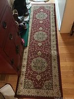 Long view of Dell Designed polypropylene runner rug with floral medallion design in burgundy and beige placed in hallway on hardwood floor next to a shoe rack.