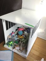 Side view of the white wooden dog cage used as a side table, missing front door, containing plush toys (not included).