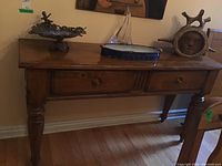 Angled view of wooden sideboard showing two drawers, turned legs, and surface wear.
