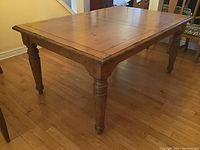 Solid wood rectangular dining table with turned legs and natural wood finish.