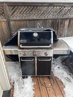 Front view of grill with closed lid, stainless steel side shelves, three control knobs, and caster wheels.