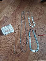 Group of five necklaces including mixed media styles and decorative seashell box on wood floor.
