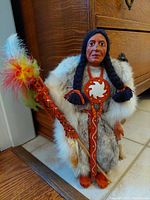 Close-up photo of a vintage handcrafted Indigenous figurine titled 'Sky Chief' in traditional dress holding a feathered staff, showing detailed sculpting and attire.