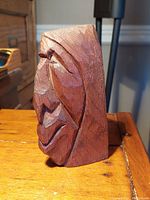 Side view of wood carving showing profile of native figure with prominent nose and lips, natural wood texture visible.