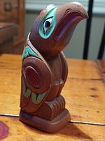 Side angle of Thunderbird totem showing hand painted eye details, green and reddish brown accents, carved feathers and smooth cultured stone material.