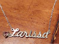 Close-up of the pendant showing the name "Larissa" in silver script with a small heart-shaped pink gemstone attached.