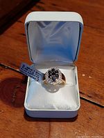 Ring in white cushioned display box showing overall presentation and condition
