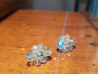 Front view of the pair of clear crystal cluster earrings showing aurora borealis sparkle and floral arrangement on a wooden surface
