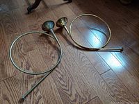 Two vintage brass decorative French horns lying on hardwood floor, showing circular coil and bell ends