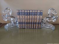 Pair of crystal glass stallion bookends holding a set of vintage books arranged vertically