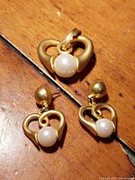 Vintage Park Lane pendant and earrings laid flat on a wooden surface. Shows gold-tone heart shapes with cultured pearls centrally positioned.
