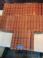Photo of 40 red hardcover Harvard Classics books with gold embossed titles on the spine arranged on a table.