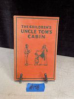 Orange cover of the book titled 'The Children's Uncle Tom's Cabin' with black illustration of three figures and text.