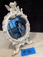 Front view of antique cast iron vanity mirror showing Cupid figure at top and ornate frame painted white.