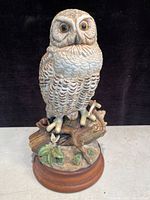 Front view of the ceramic owl figurine showing detailed feathers, large eyes, branch with leaves and flower, and wooden base.