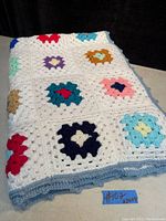 Folded view of the crochet throw showing colorful granny squares and light blue trim edge.