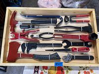 Top-down view of the custom wooden box containing assorted vintage hand tools with red and black handles, arranged for display.