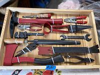 Top view of various vintage hand tools neatly arranged and secured inside a custom wooden box with elastic bands.
