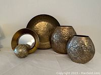 Display of all brass items including two vases with embossed floral design, hammered brass shallow bowl, mirrored-bottom bowl, and covered box.