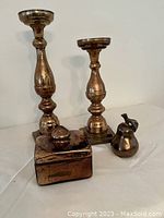 Pair of copper-colour candle holders, rectangular decorative box with lid, and pear decorative piece arranged together showing reflective, antiqued finish.
